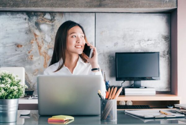 Woman sitting at desk in front of an open laptop talking on a cell phone